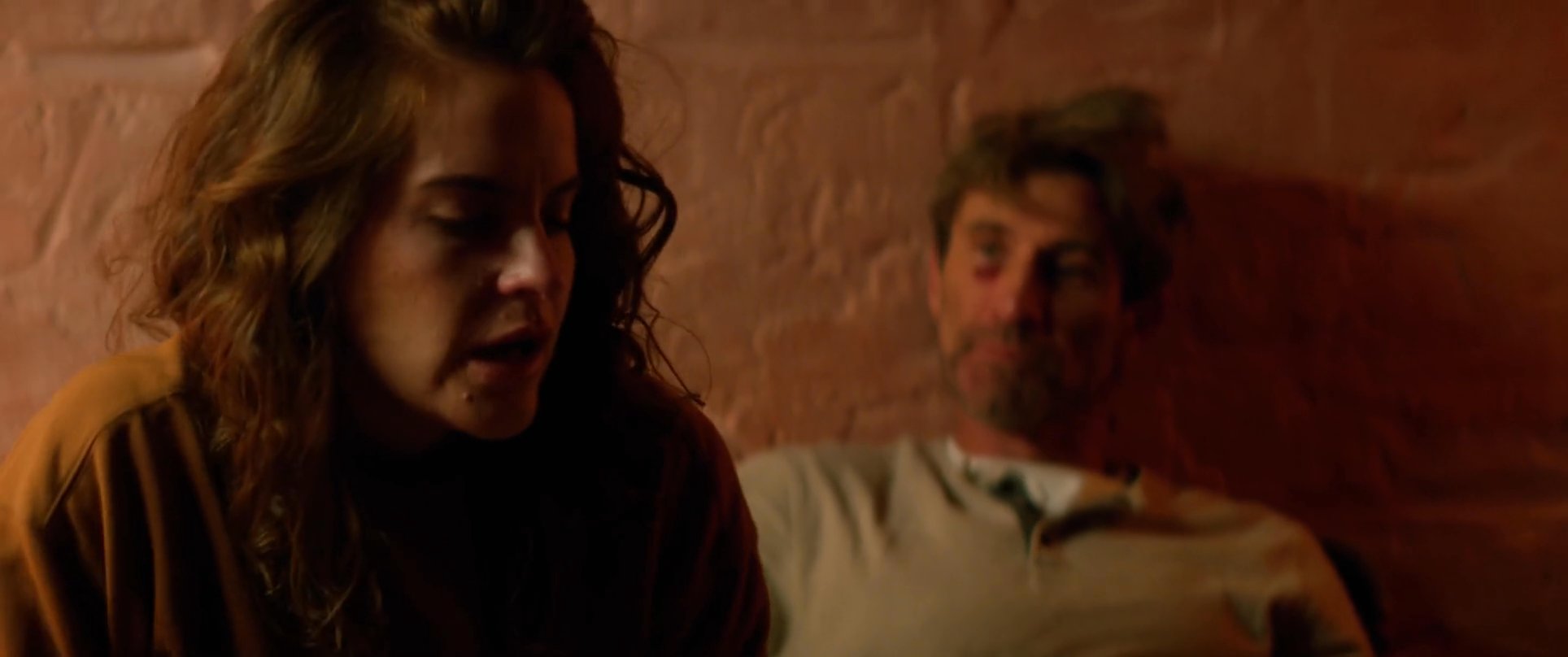 A couple sits together in a dimly lit, warm environment, transitioning from intimate physical closeness to an engaged, thoughtful conversation.