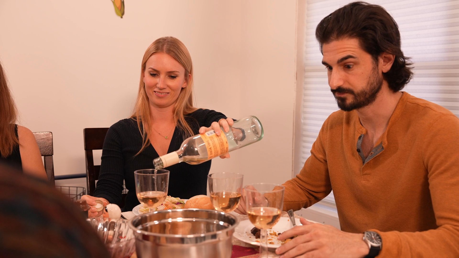 Friends and family gather around a dining table decorated with festive food to share a meal and wine during a holiday celebration. Participants engage in conversation while enjoying the prepared feast.