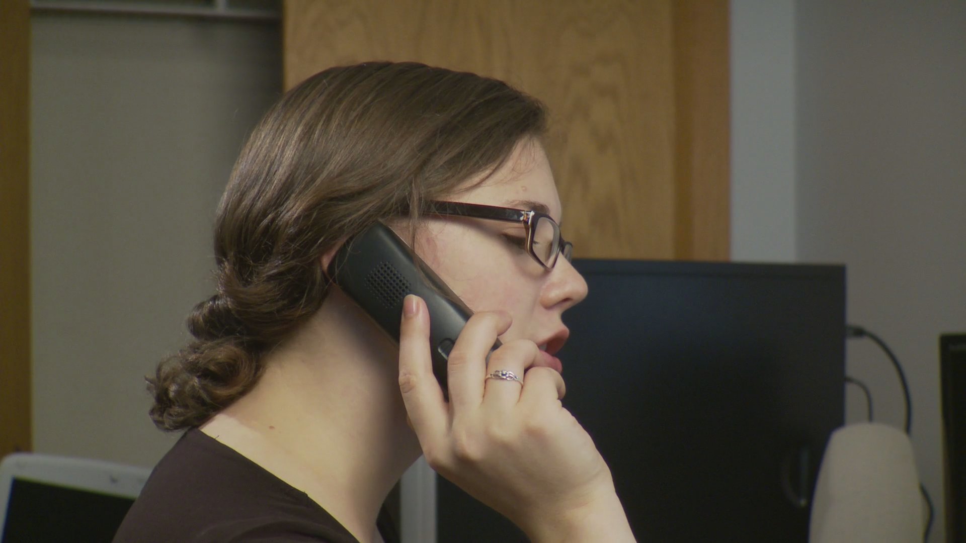 Two individuals conduct separate telephone conversations within a professional office environment, focusing on information exchange and task coordination.