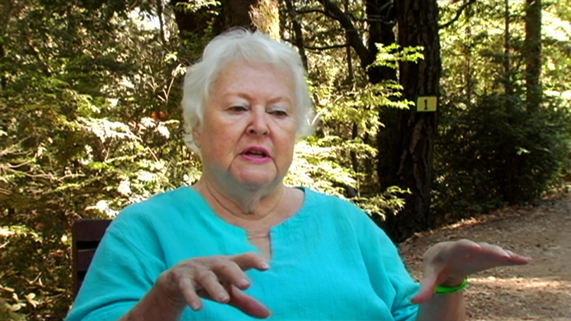 An older woman shares a personal story in a forest setting, followed by a conversation with two long-haired motorcyclists sitting on their bikes.