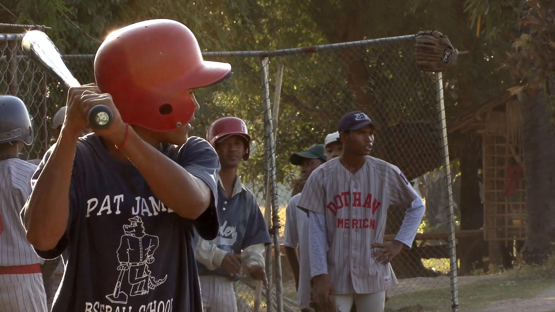 Coaches provide instruction and mentorship to a team of young baseball players on a sunlit field. The session includes batting practice, defensive positioning, and active team engagement.