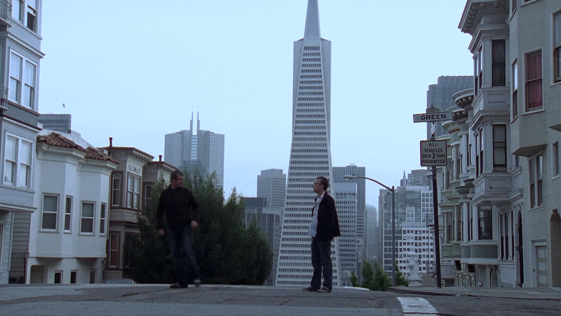 Two individuals engage in a brief conversation on a hillside street in San Francisco. Following their interaction, one person departs in a blue vehicle.