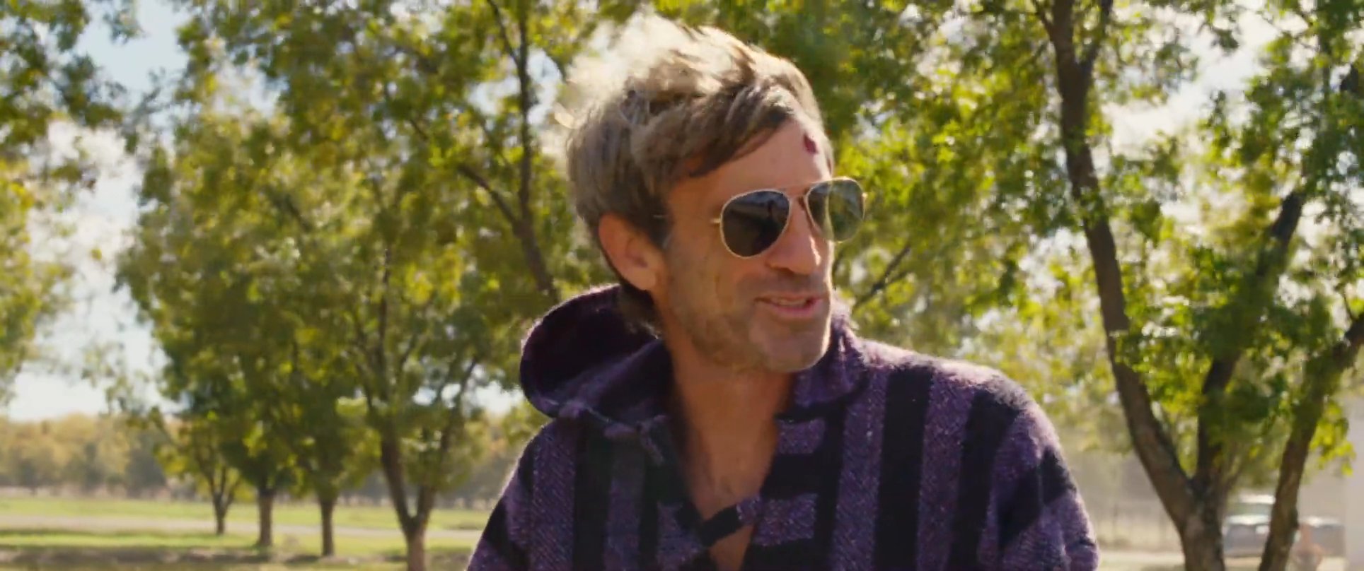 Two men engage in an earnest conversation while standing in a bright, tree-lined outdoor setting. They exchange perspectives with clear focus and expressive facial gestures.