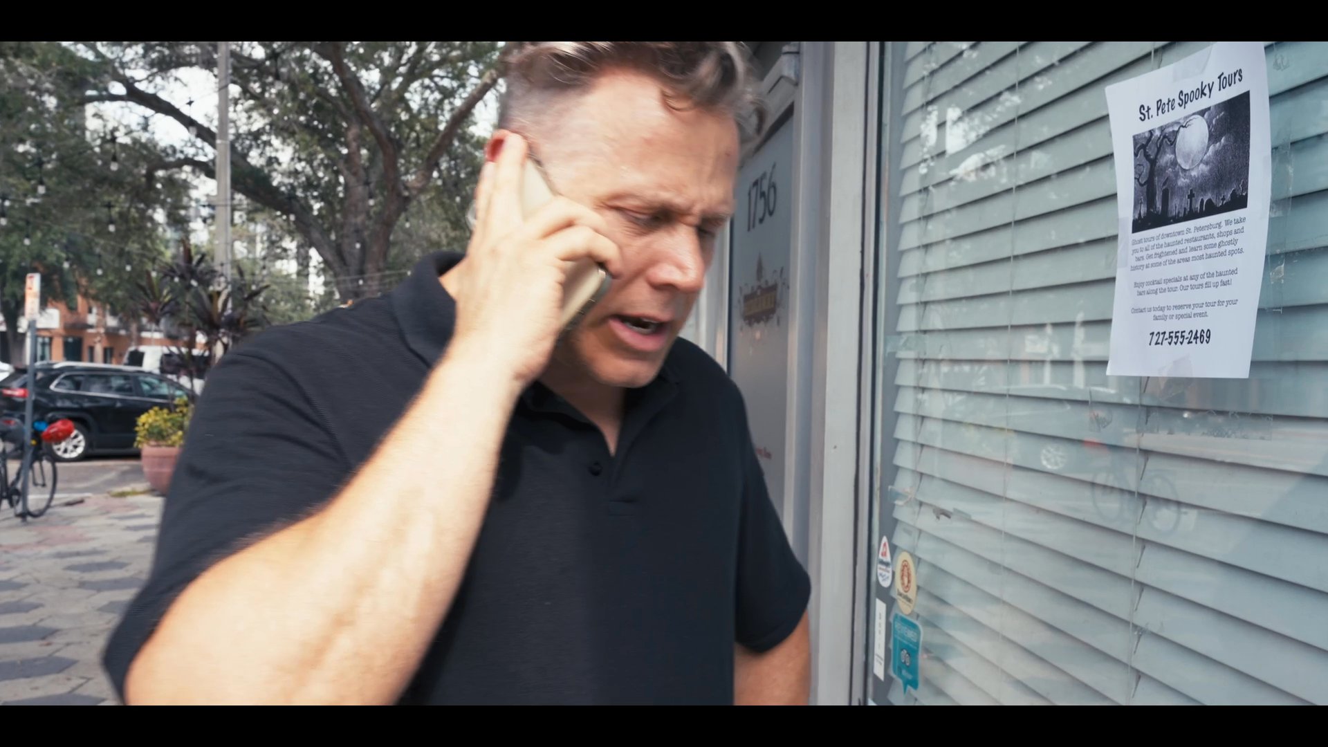 A man stands on a city sidewalk while engaged in a focused telephone conversation.