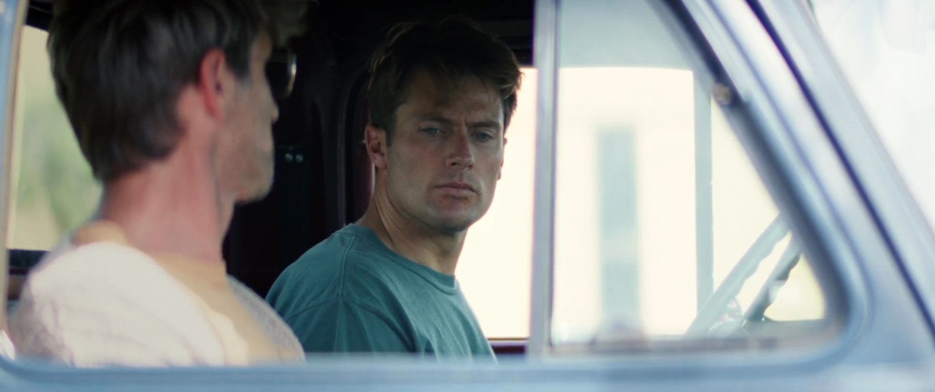 Two men engage in a tense, focused conversation while sitting inside a vehicle.