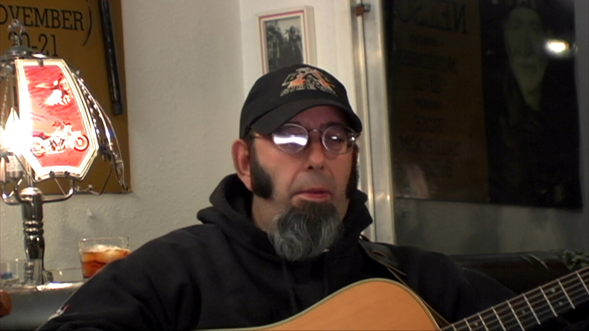 Patrons socialize in a motorcycle-themed bar while a musician performs acoustic music. The scene transitions between the lively atmosphere of the bar and the guitarist's performance.