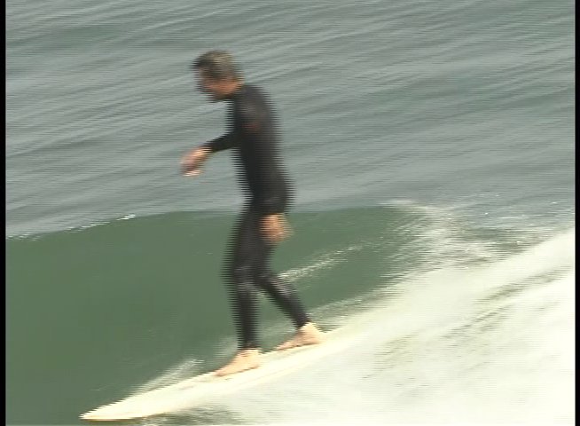 A surfer in a wetsuit skillfully maneuvers a longboard along the face of an ocean wave.