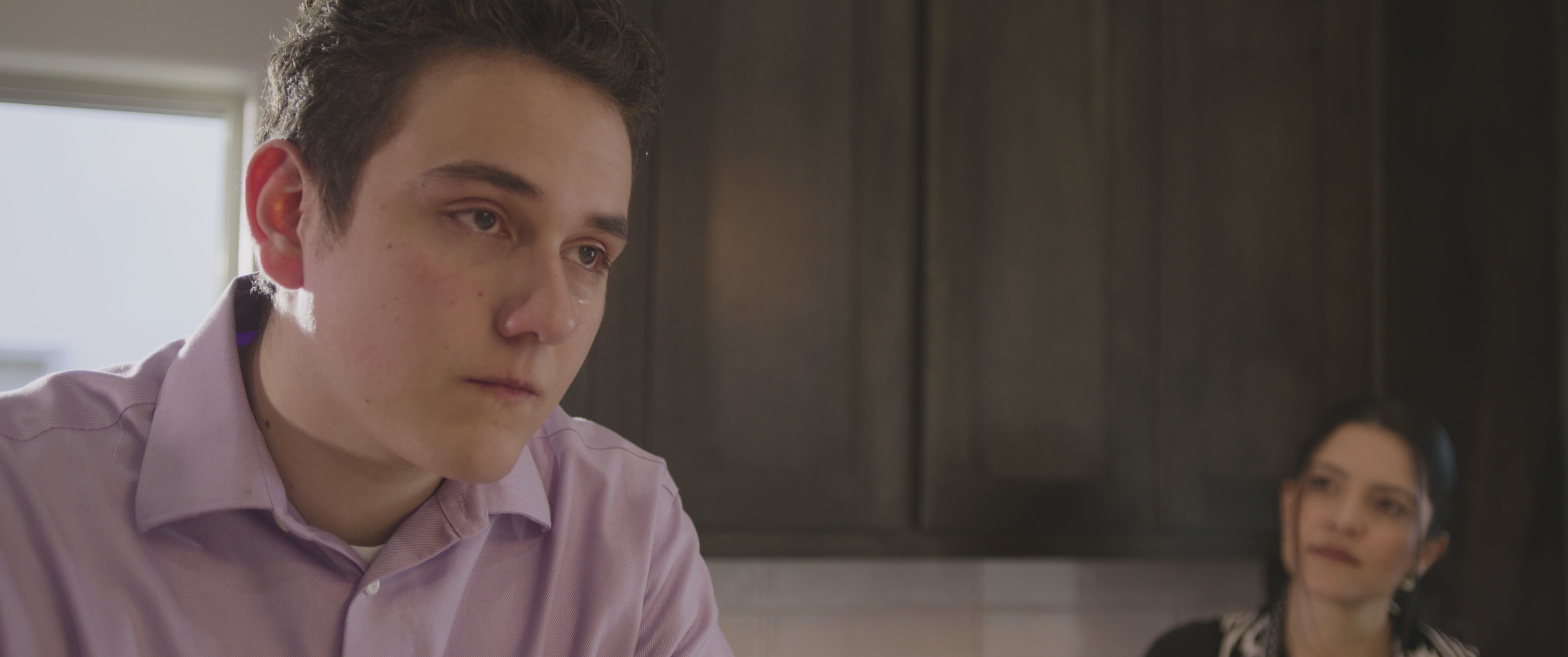 A young man and a woman engage in a quiet conversation within a home kitchen while the woman drinks from a reusable water bottle.