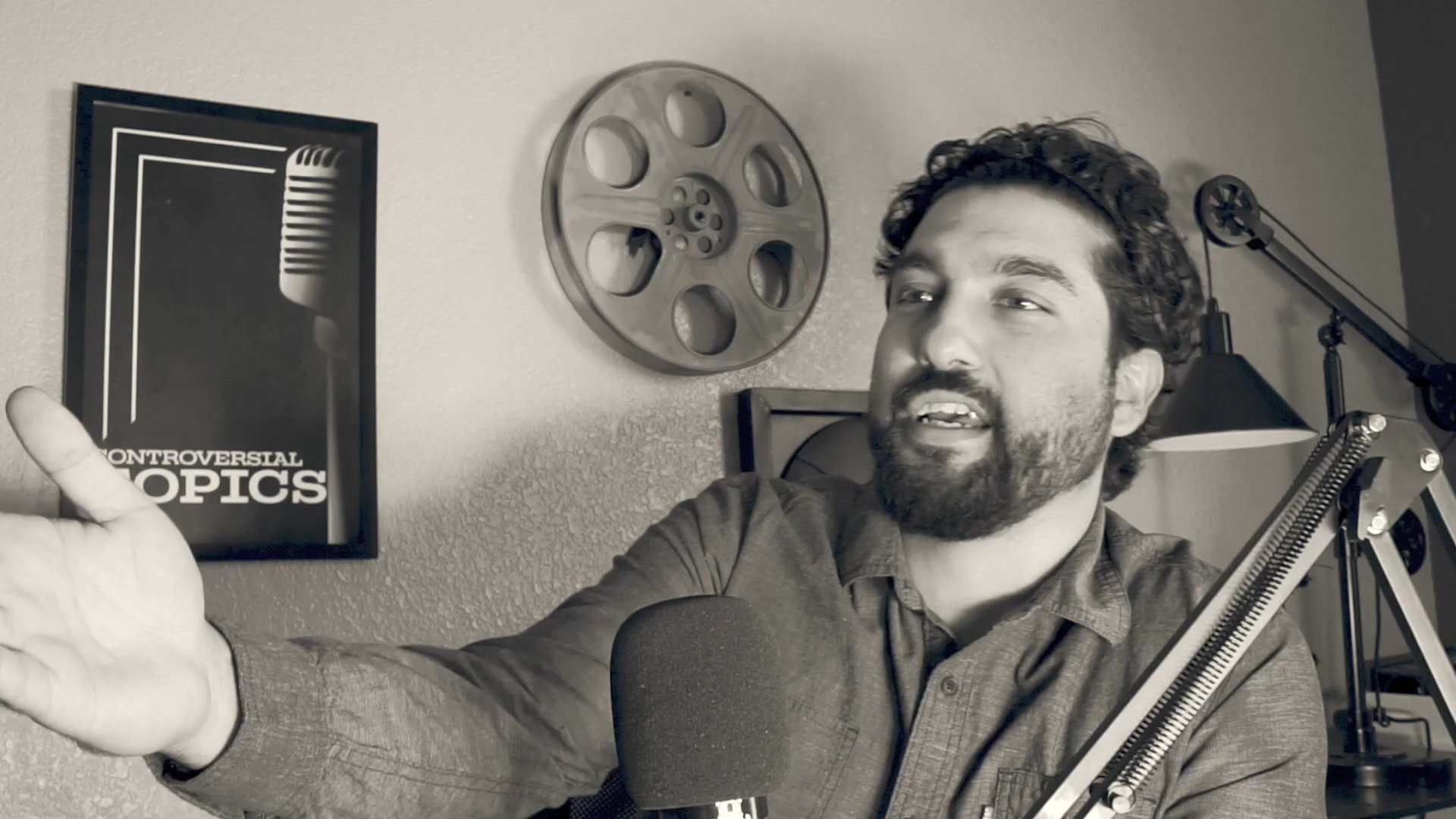 A man speaks directly into a microphone in a studio setting, using expressive hand gestures and facial expressions to convey his narrative. The scene captures an intimate moment of personal storytelling or insightful commentary.