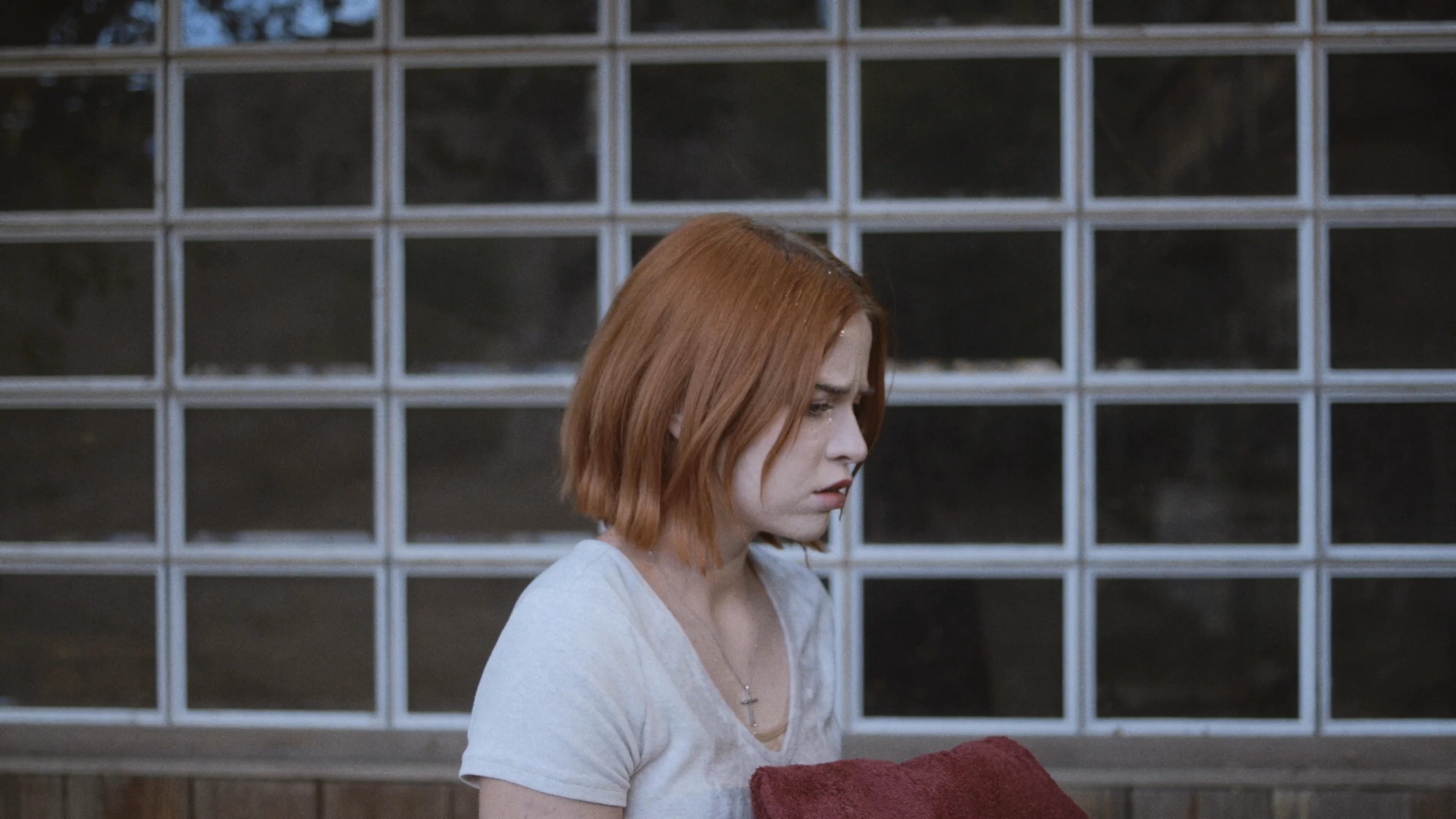 A woman exhibits visible signs of apprehension and unease while monitoring her environment, shifting between a starkly lit interior space and a reflective moment at a vanity.