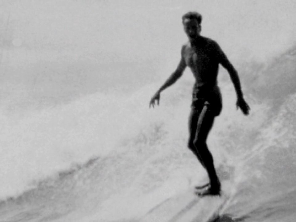 An elderly surfer reflects on his past as archival black-and-white footage transitions from his current interview to scenes of him riding waves in his youth.