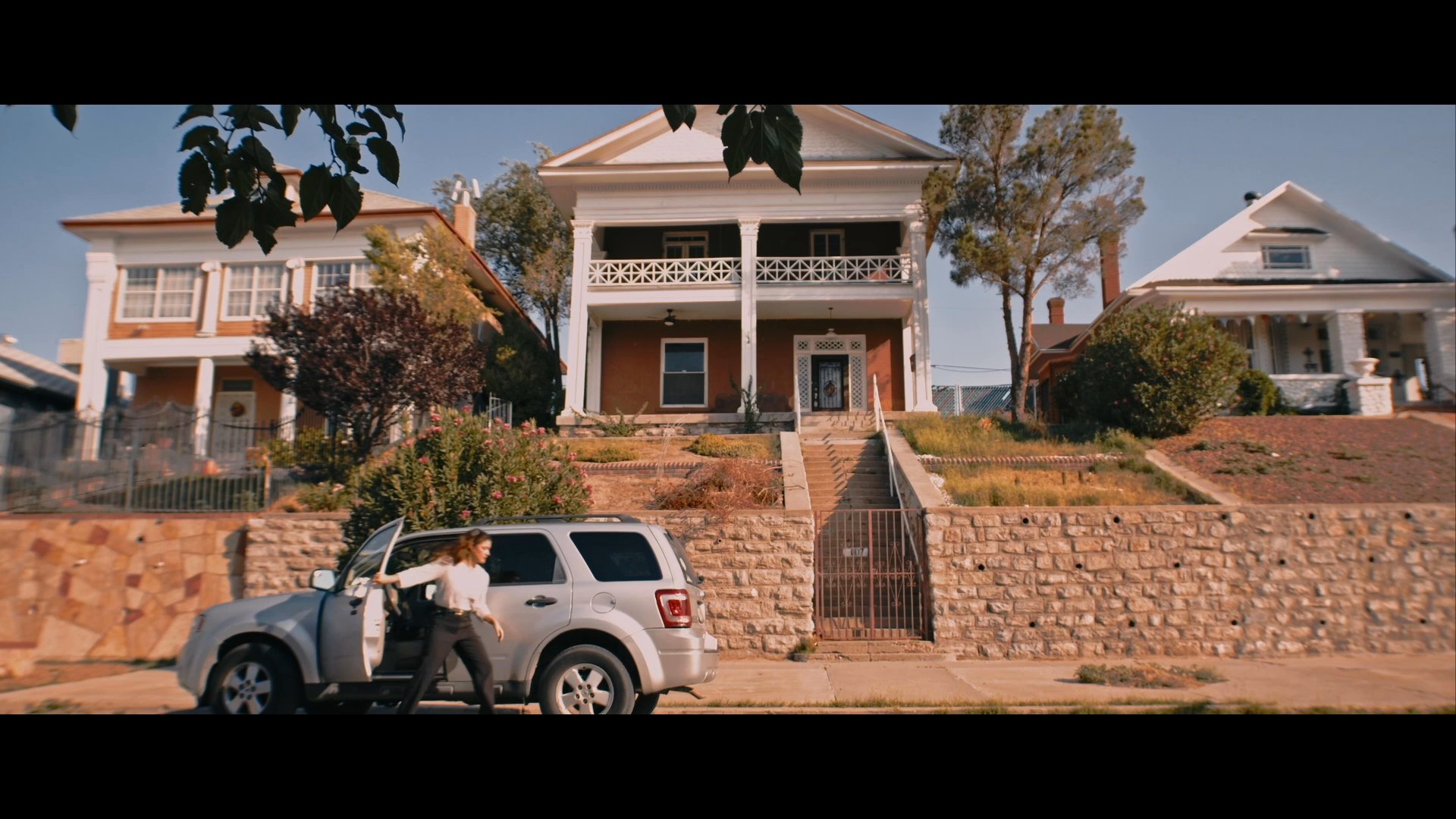 A woman concludes a telephone conversation while arriving at a suburban residence in her SUV. She exits the vehicle and walks toward the house.