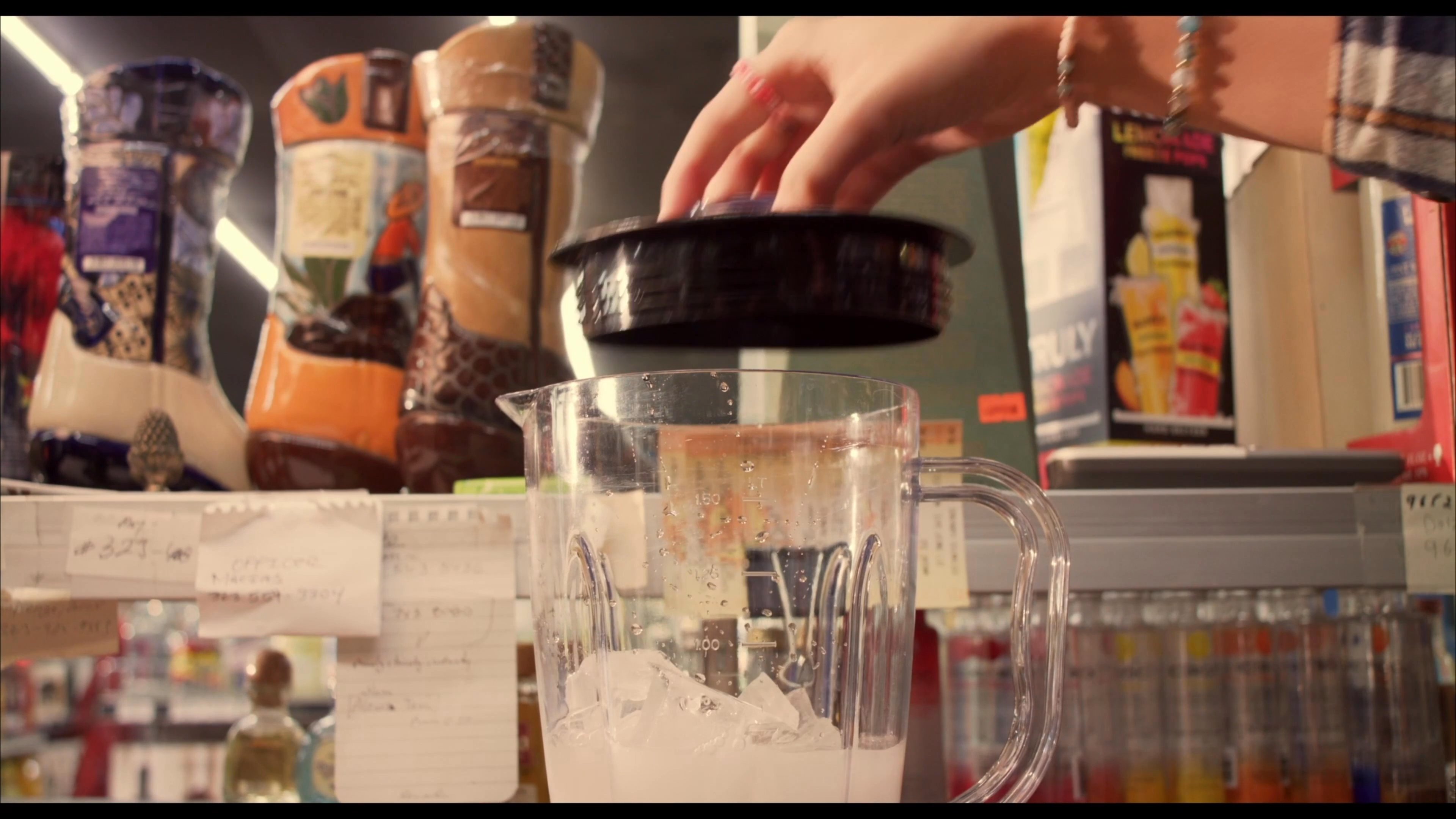 A man and a woman prepare a frozen beverage inside a liquor store by combining ice and ingredients in a blender.