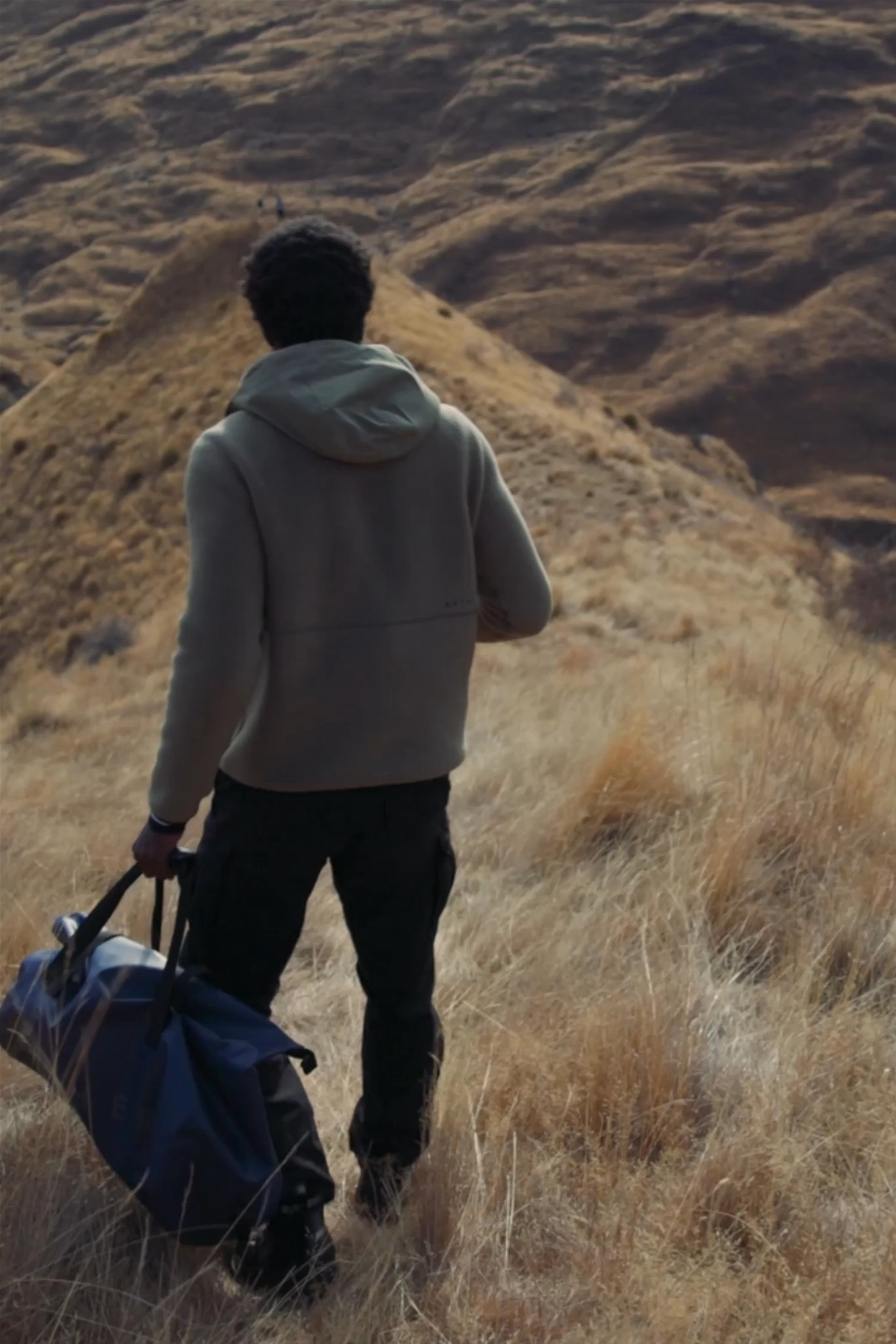 Man walking down a hill; man loading luggage into the trunk of a car