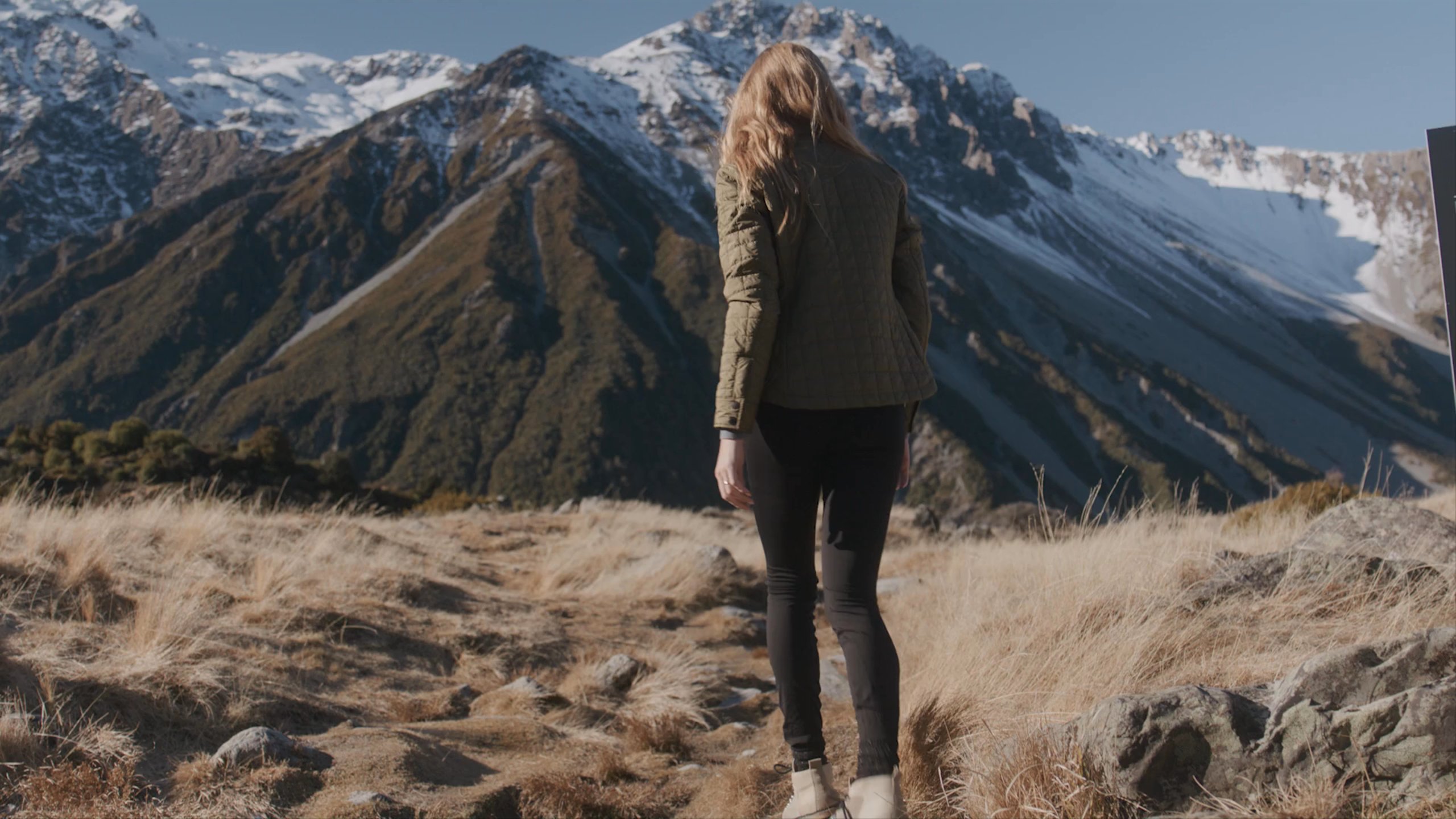 A woman relaxing on a walk in the foothills of New Zealand, sitting and relaxing with a friend.