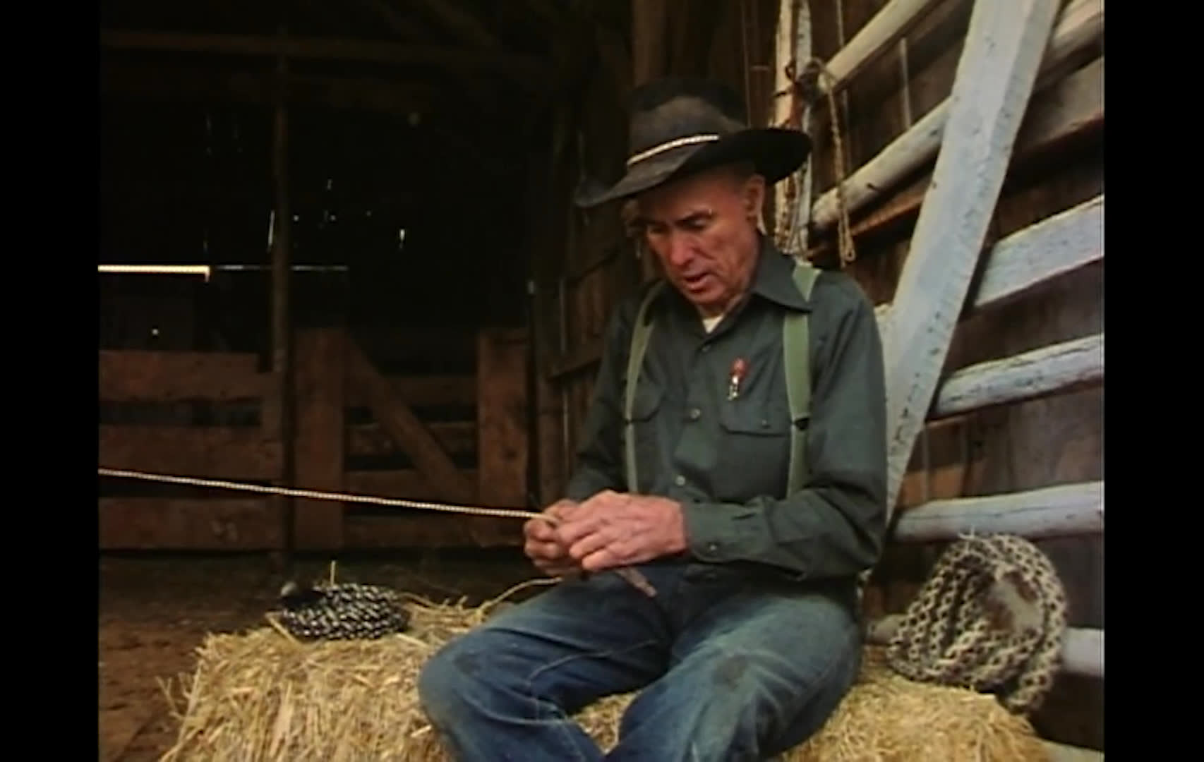 A hat-wearing rancher sits in a weathered barn, handling a thin cord as he reflects on riding through sagebrush beneath granite spires. The sequence closes on a dusky rural road at sunset, echoing his appreciation for the trail.