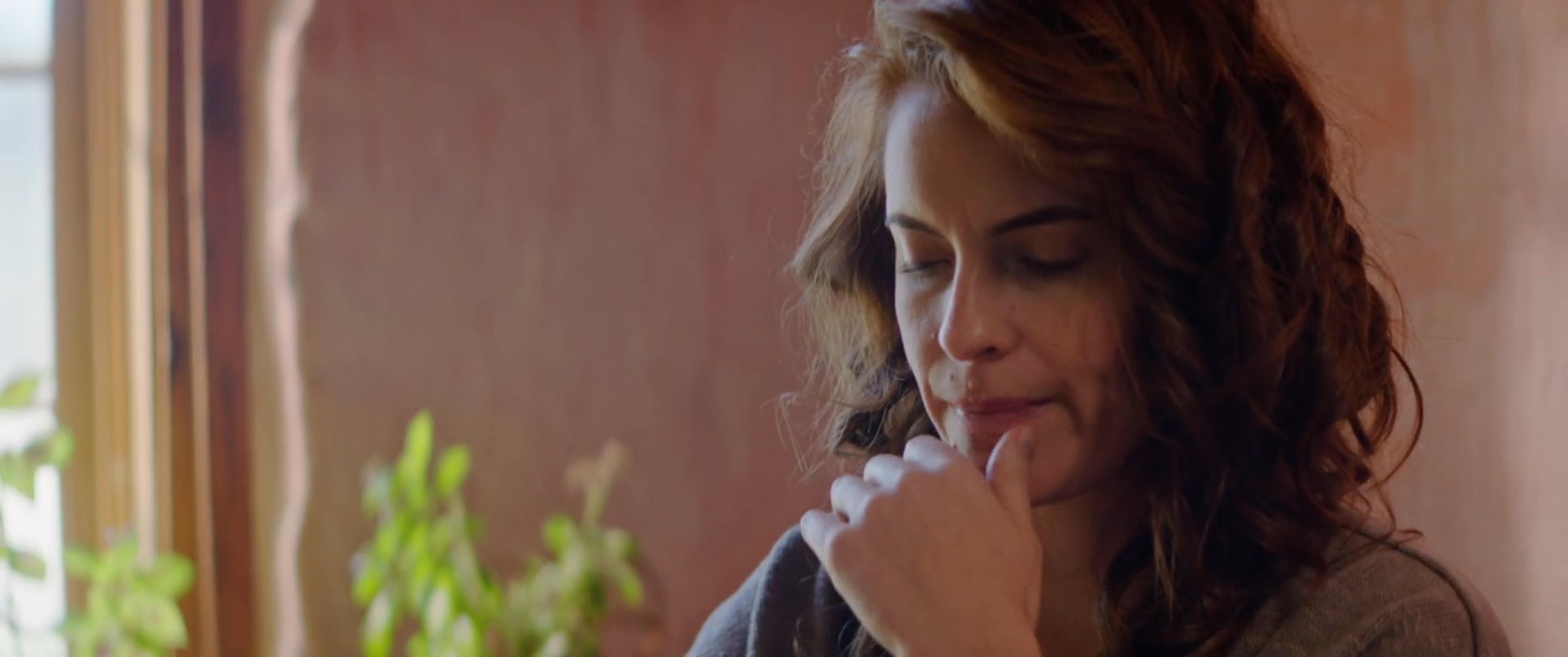 A man and woman share an intimate conversation while holding hands at a table in a sunlit room. Their interaction shifts from quiet connection to a focused exchange, reflecting a moment of emotional depth.