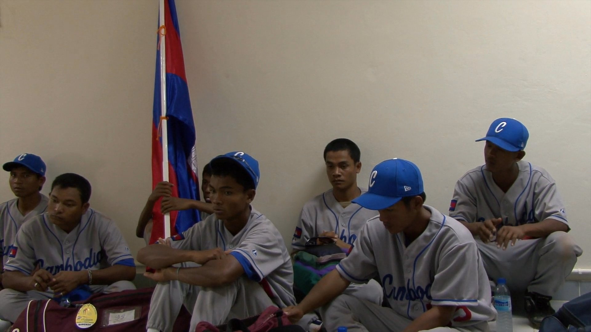 A baseball coach delivers a motivational strategy talk to his players, emphasizing error reduction and collective resilience during an indoor team meeting.