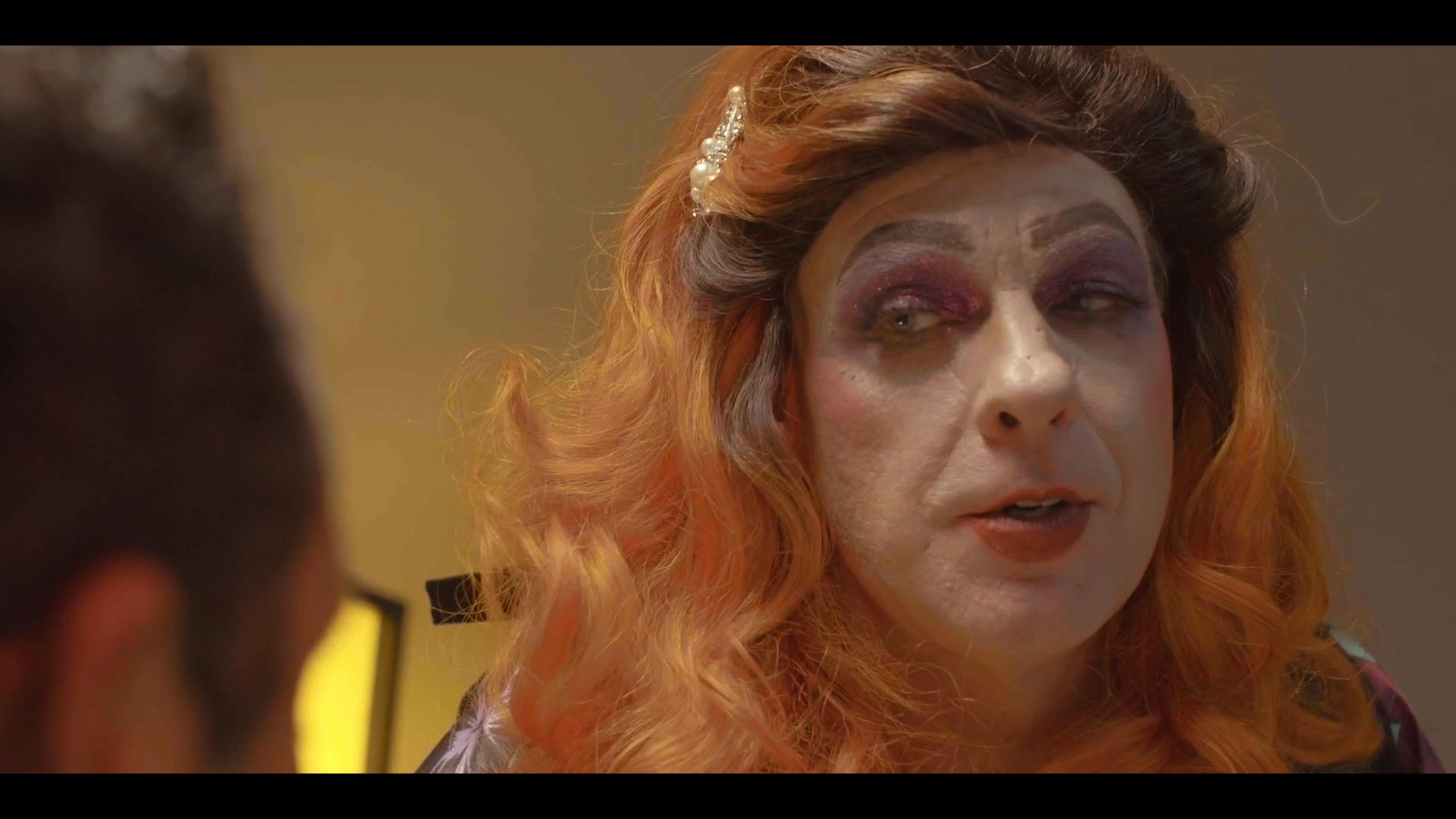 A performer in drag engages in an intense conversation with a man, leading to a transition where an individual emotionally consumes food while crying.