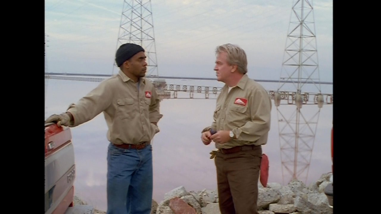 Two utility technicians discuss technical project details while standing beside a pickup truck near high-voltage power transmission lines.