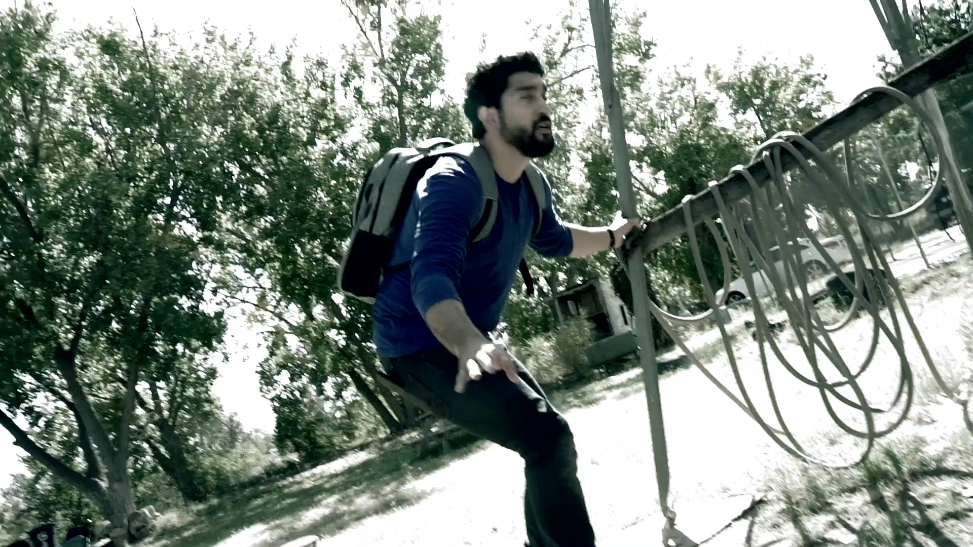 A man wearing a backpack prepares and launches a drone in an outdoor park setting for aerial photography.