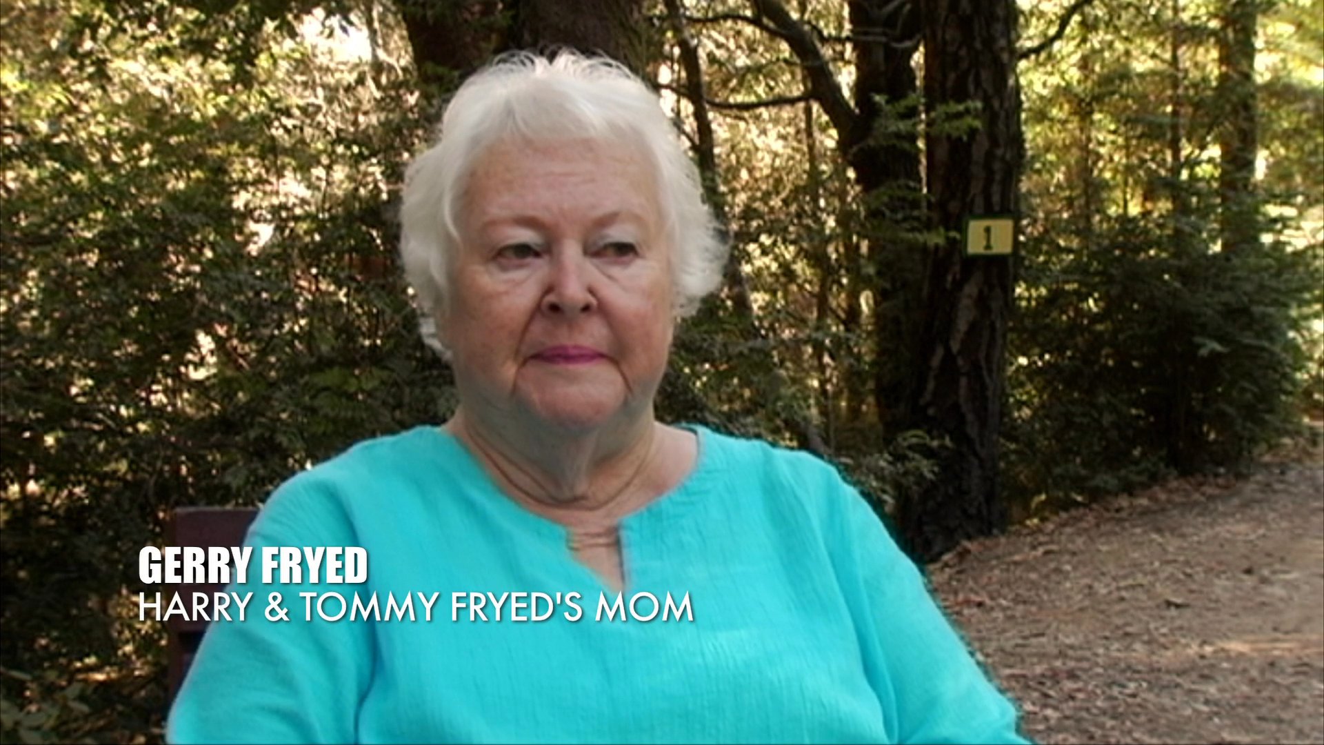 Gerry Fryed recounts family memories while vintage home movie footage illustrates her narrative. The sequence contrasts her present-day reflections with past moments captured on film.