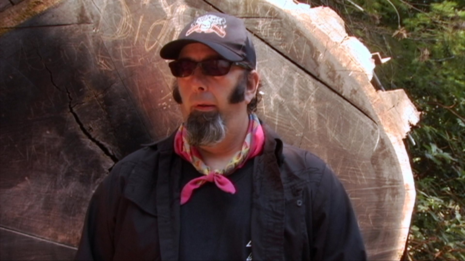 A man wearing a hat and sunglasses discusses music in an outdoor setting, followed by a transition to a two-man band playing an acoustic guitar and a violin indoors.