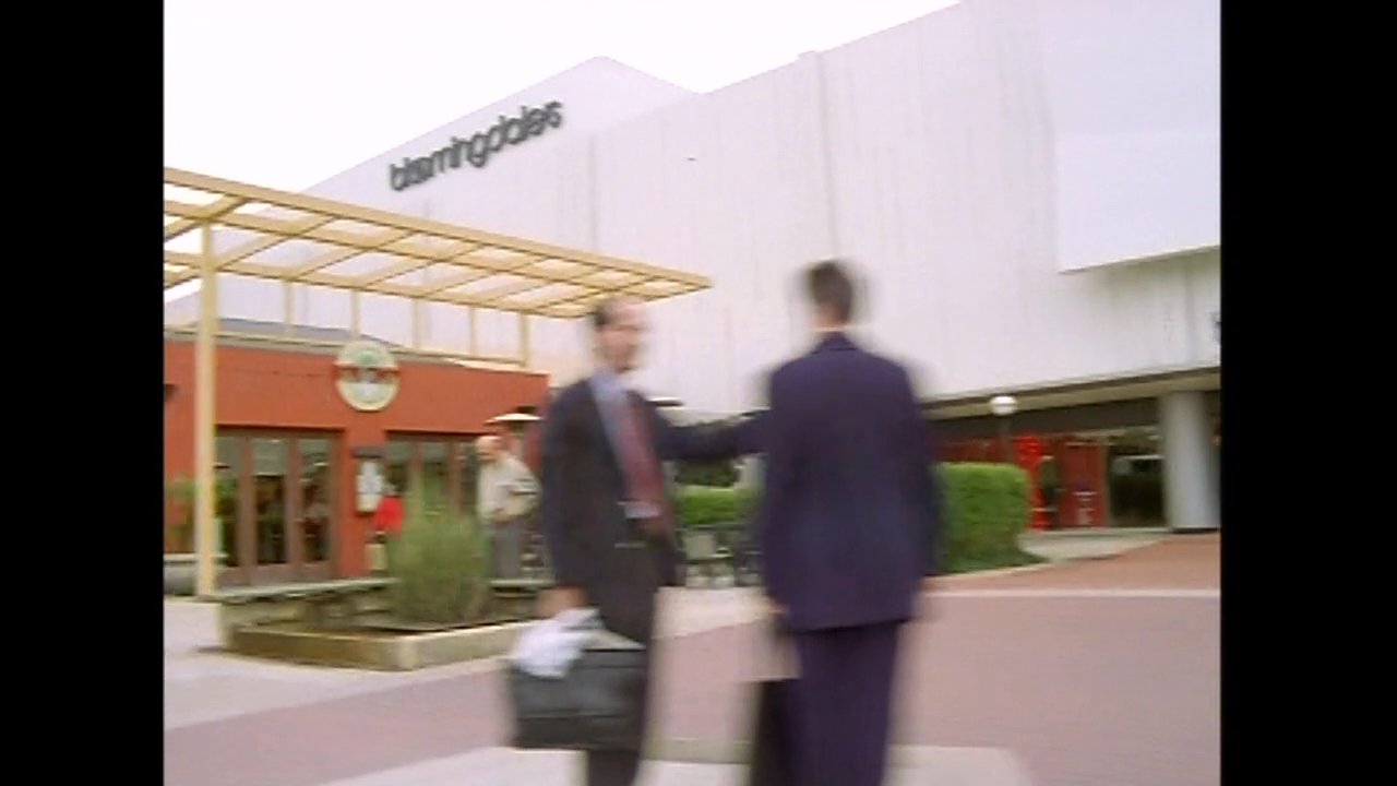 A man and woman drive through a suburban area before arriving at a shopping center. The pair continues their conversation while traveling toward the commercial destination.