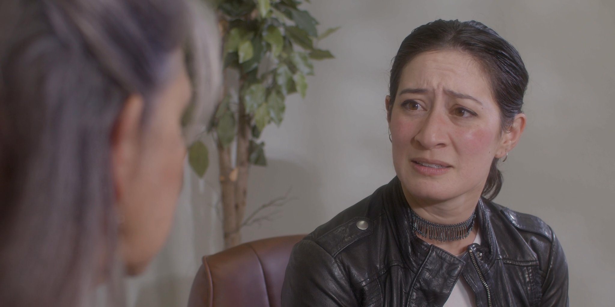 Two women engage in an intimate, serious conversation, sharing personal experiences in a professional or therapeutic setting. Their expressions shift between empathetic listening and vulnerable articulation.