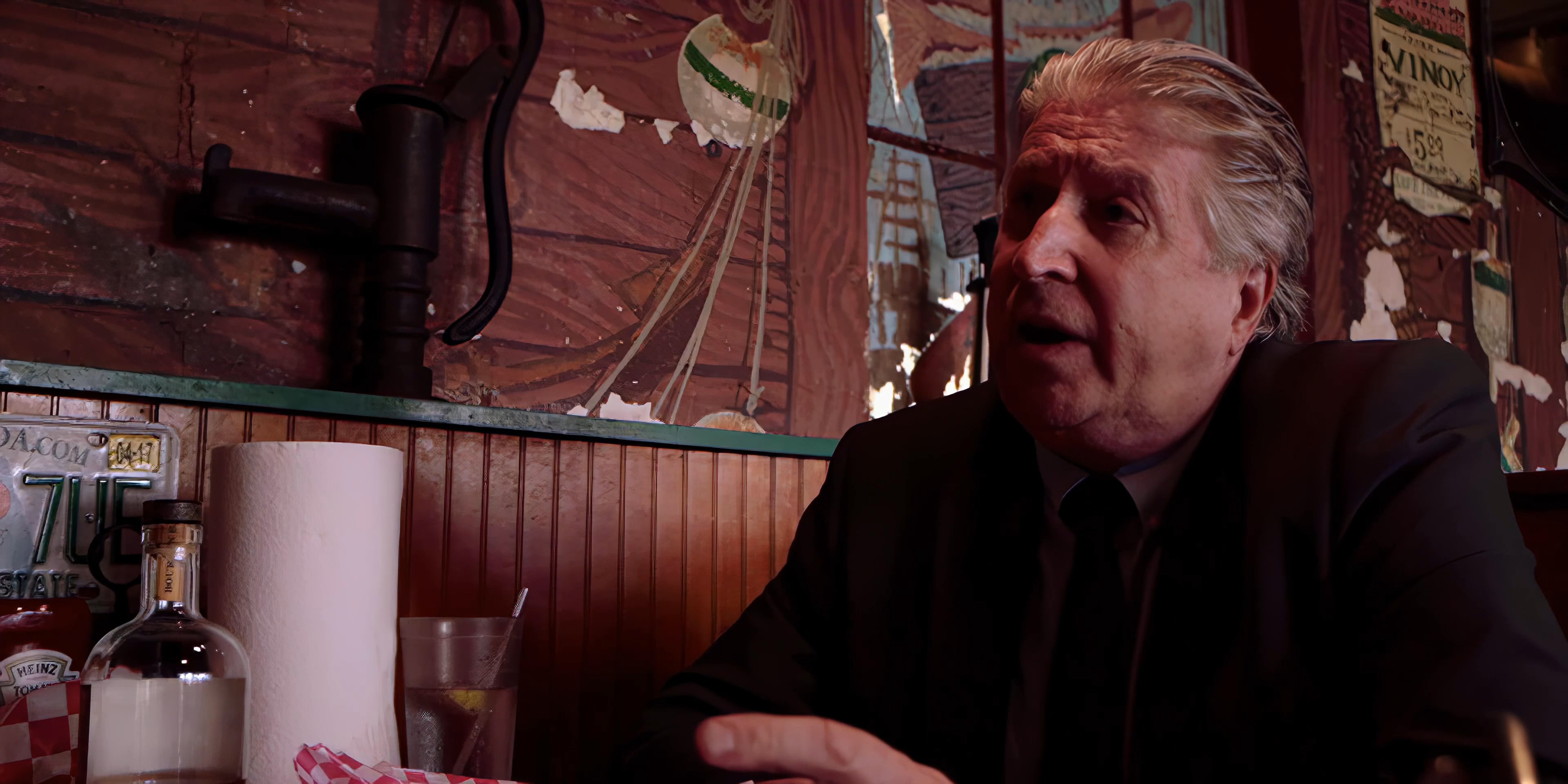 Two men engage in a serious, focused conversation while seated across from each other in a rustic, wood-paneled diner booth.