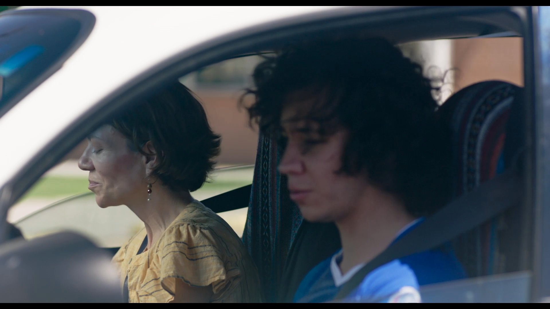 A woman provides guidance to a student driver as they sit together in a vehicle. The pair engages in a calm, instructional conversation during a training session.