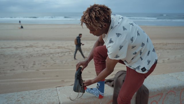 A young man putting shoes on at the beach