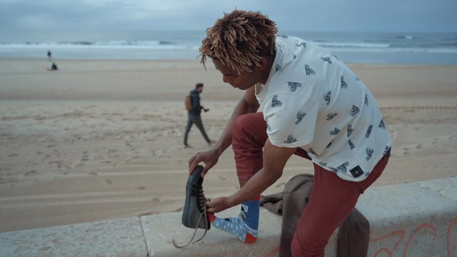 A young man putting shoes on at the beach
