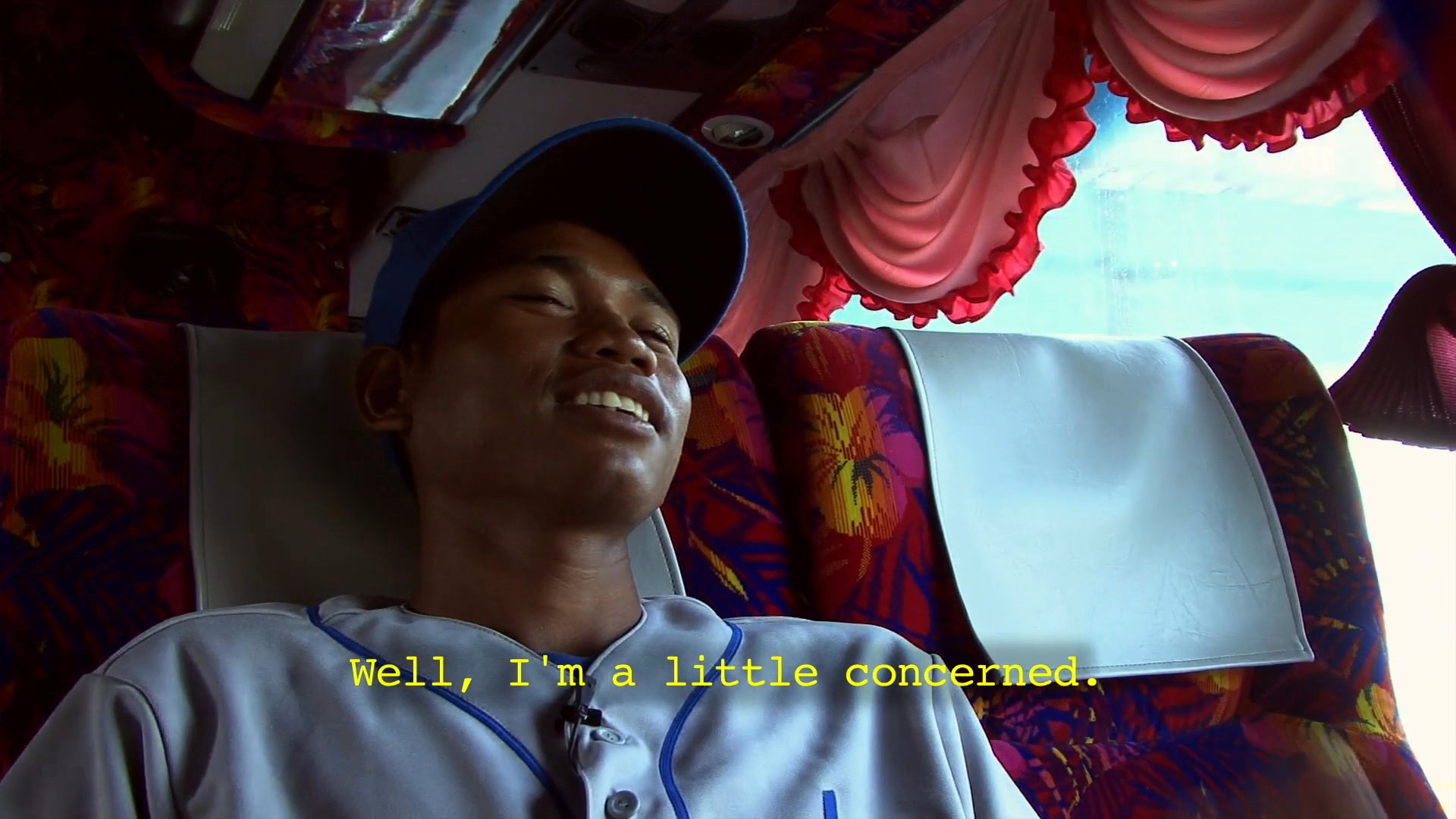 An athlete wearing a baseball jersey shares his thoughts and concerns regarding upcoming SEA Games competition while sitting on a bus. He reflects on playing against other teams and expresses his apprehension about potential match outcomes and team reactions.