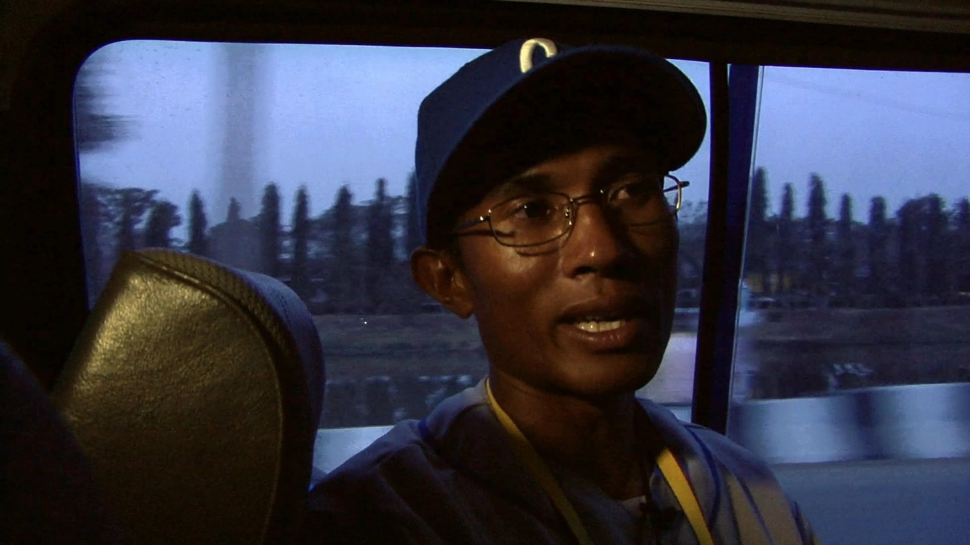 A baseball player in uniform discusses his experiences while transitioning between a stadium setting and traveling by bus.