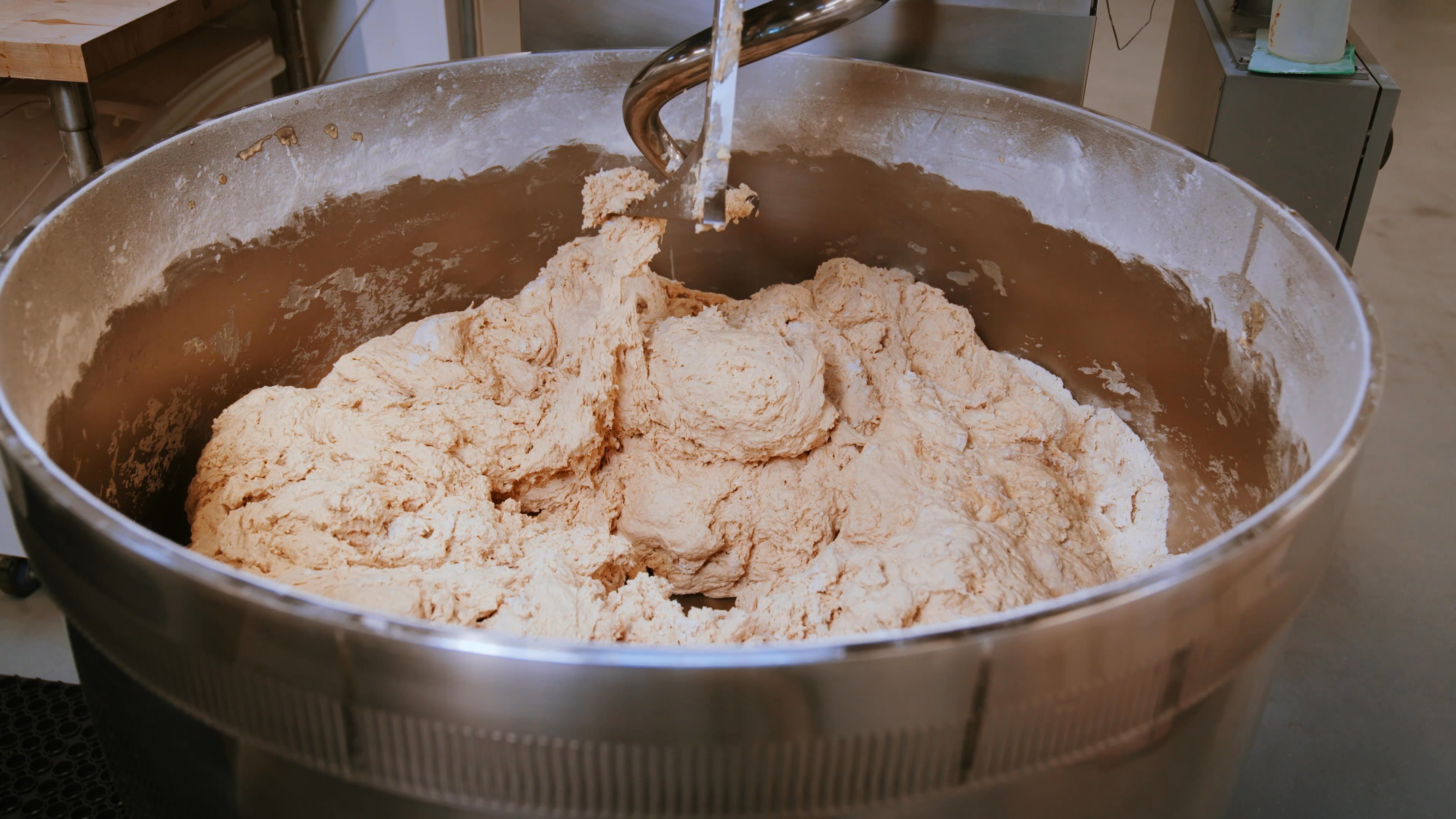 An industrial manufacturing system processes bulk ingredients and mixes dough before moving it along an automated conveyor line for portioning. The operation demonstrates efficient, large-scale commercial baking techniques.