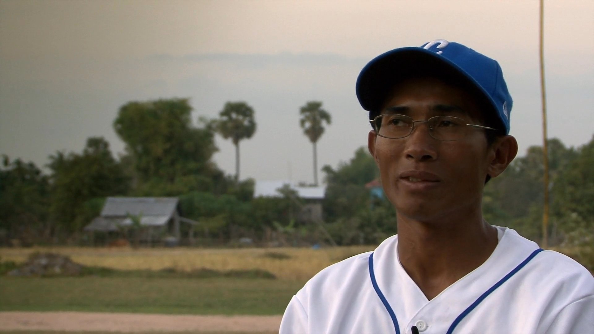 An athlete practices pitching mechanics on a rural field before sharing insights during an interview about his baseball development.