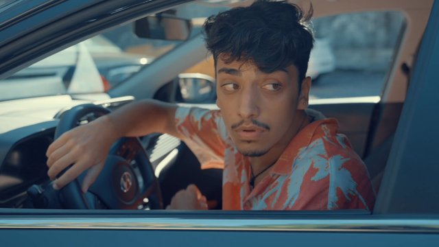 A teenage boy tiredly looking for someone out of his car window