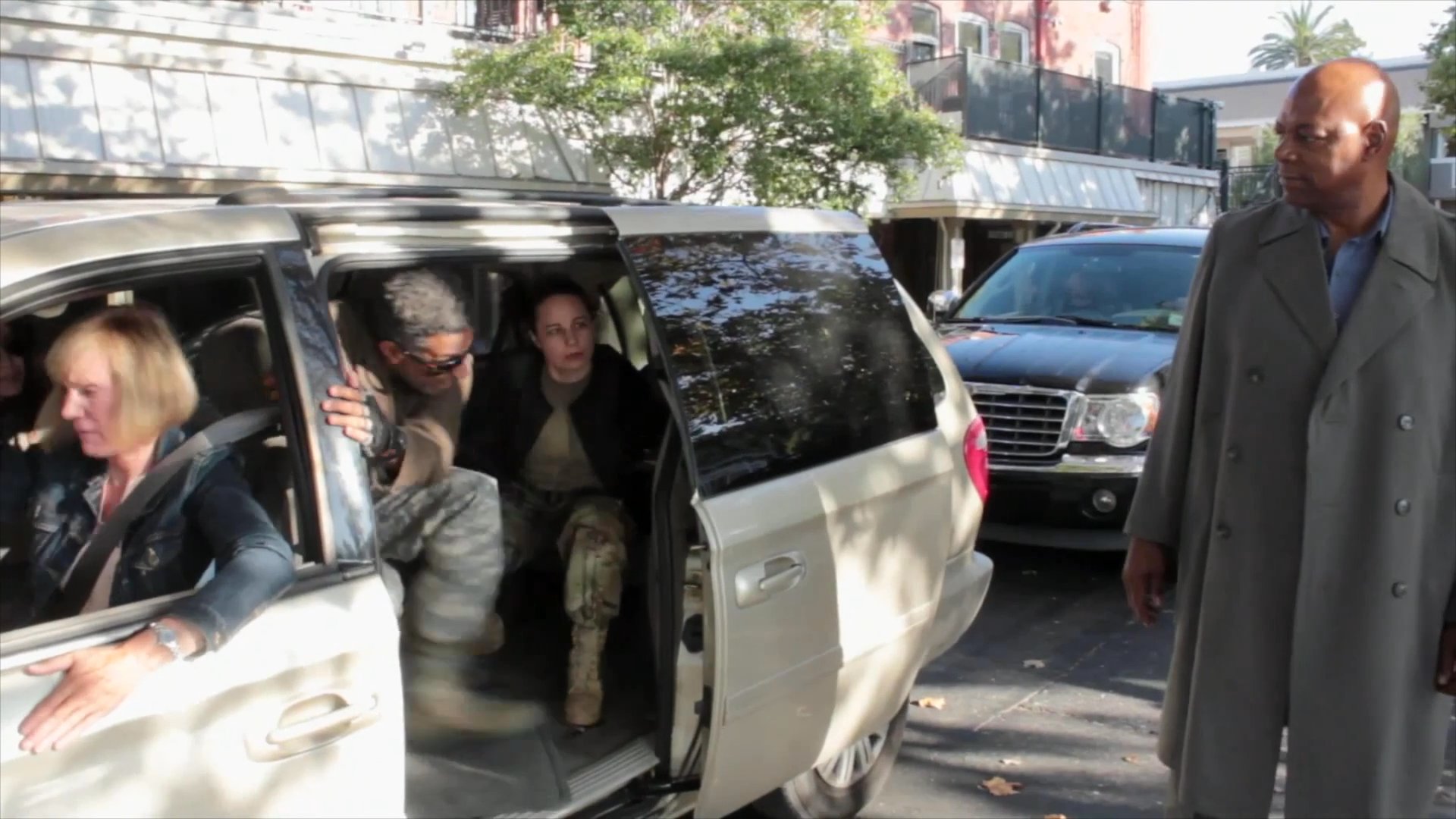 Two men engage in a brief discussion on a city street before one coordinates the departure of passengers from a minivan.