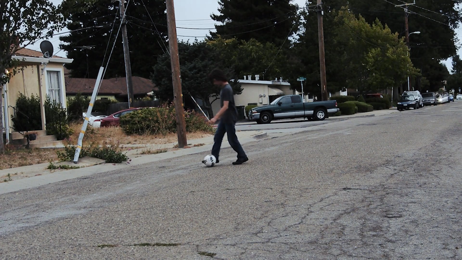 A young individual practices soccer ball control and dribbling maneuvers on a quiet residential street. The scene captures the athlete navigating the ball forward with consistent footwork.