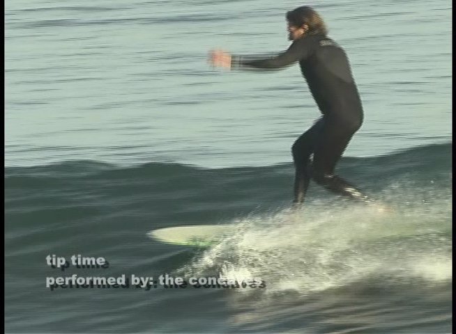 A skilled surfer wearing a wetsuit rides a longboard along the face of a gentle ocean wave. The athlete maintains balance while executing fluid movements on the water's surface.
