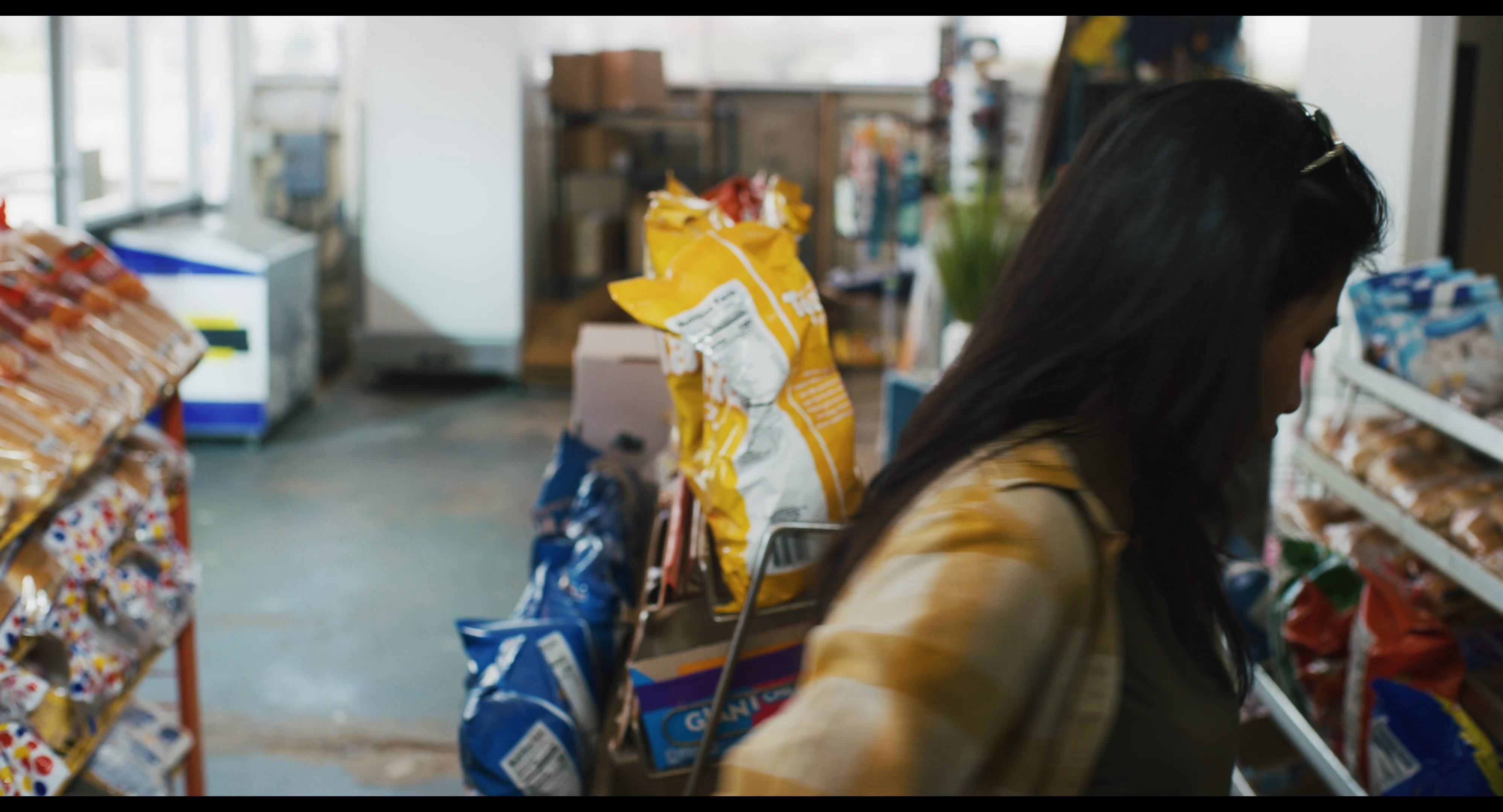 A woman walks through a small retail space, examining photographs displayed on a rack before browsing merchandise near the checkout area.