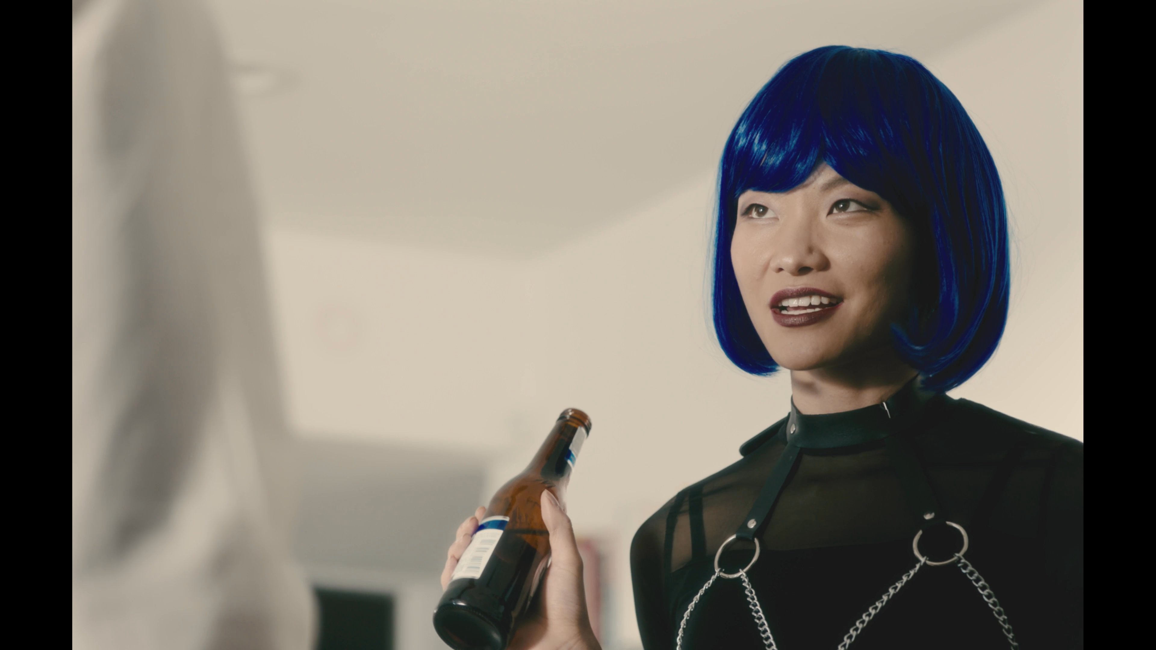 A woman wearing a blue wig engages in a tense, rhythmic conversation with a man while holding a beer bottle at a bar. The dialogue unfolds through focused exchanges and close-up reactions.