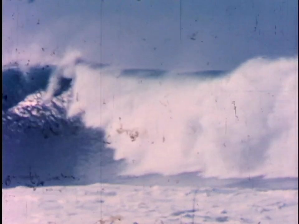 A skilled surfer maneuvers across powerful, cresting ocean waves. The sequences capture the athlete navigating the challenging swells within a vast marine environment.