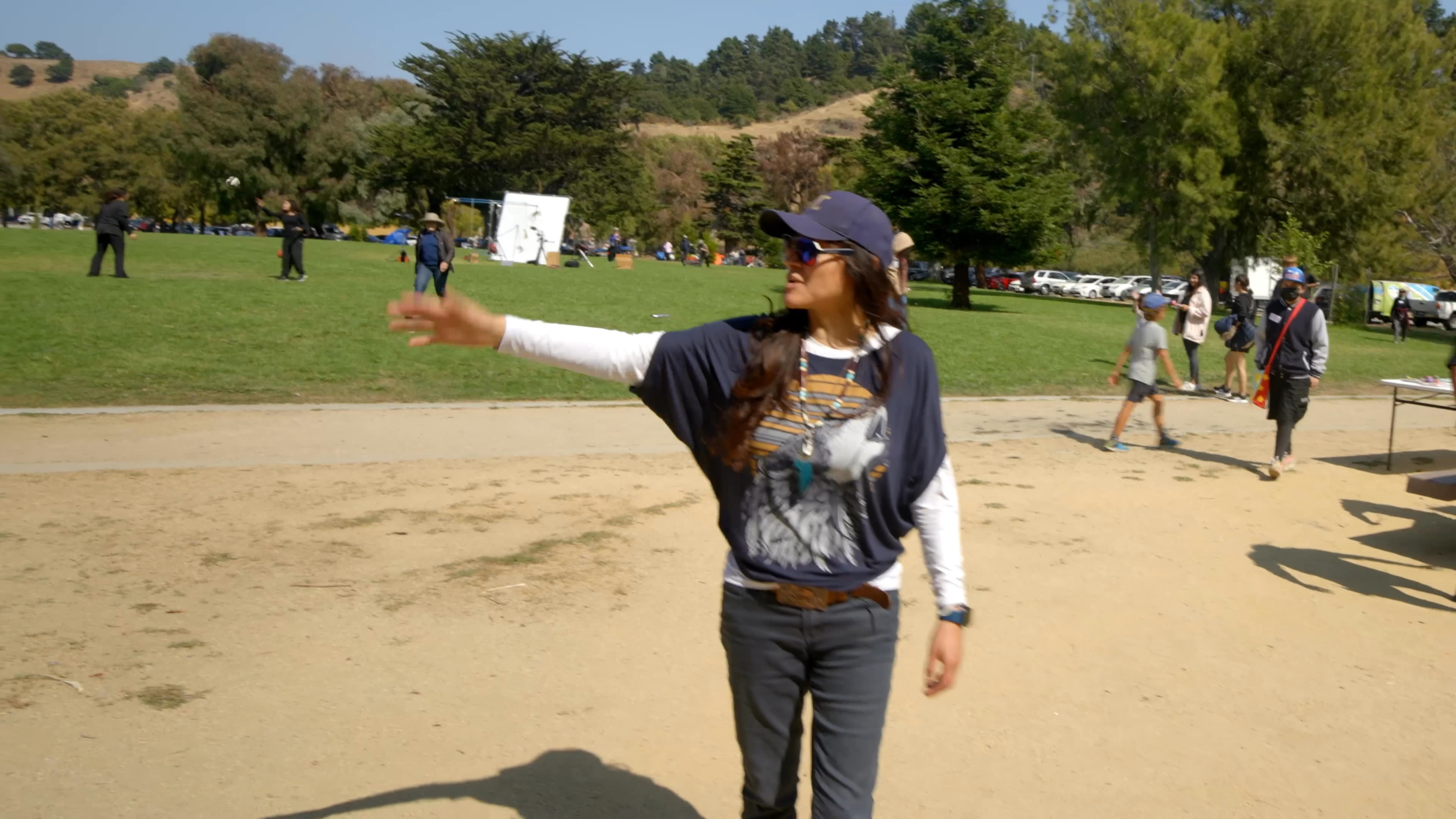 A woman reflects on discovering her identity and aspirations in college, where a professor saw beyond stereotypes associated with her immigrant background. She speaks in a park, then walks across the grounds and greets people gathered nearby.