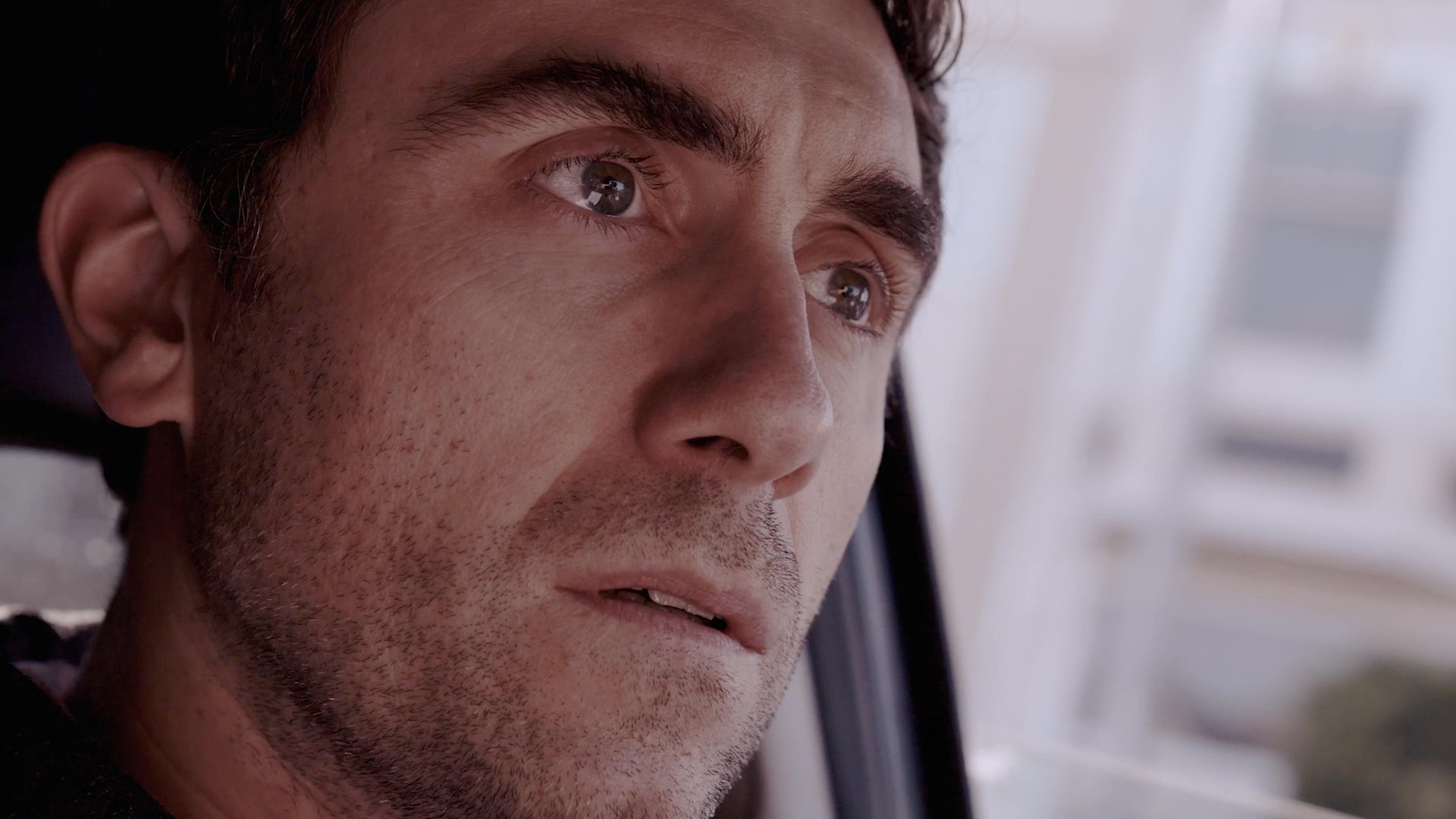 A man watches from a car as another man proposes to a woman at an outdoor restaurant table. The sequence alternates between the intimate proposal scene and the observer's watchful, contemplative gaze.