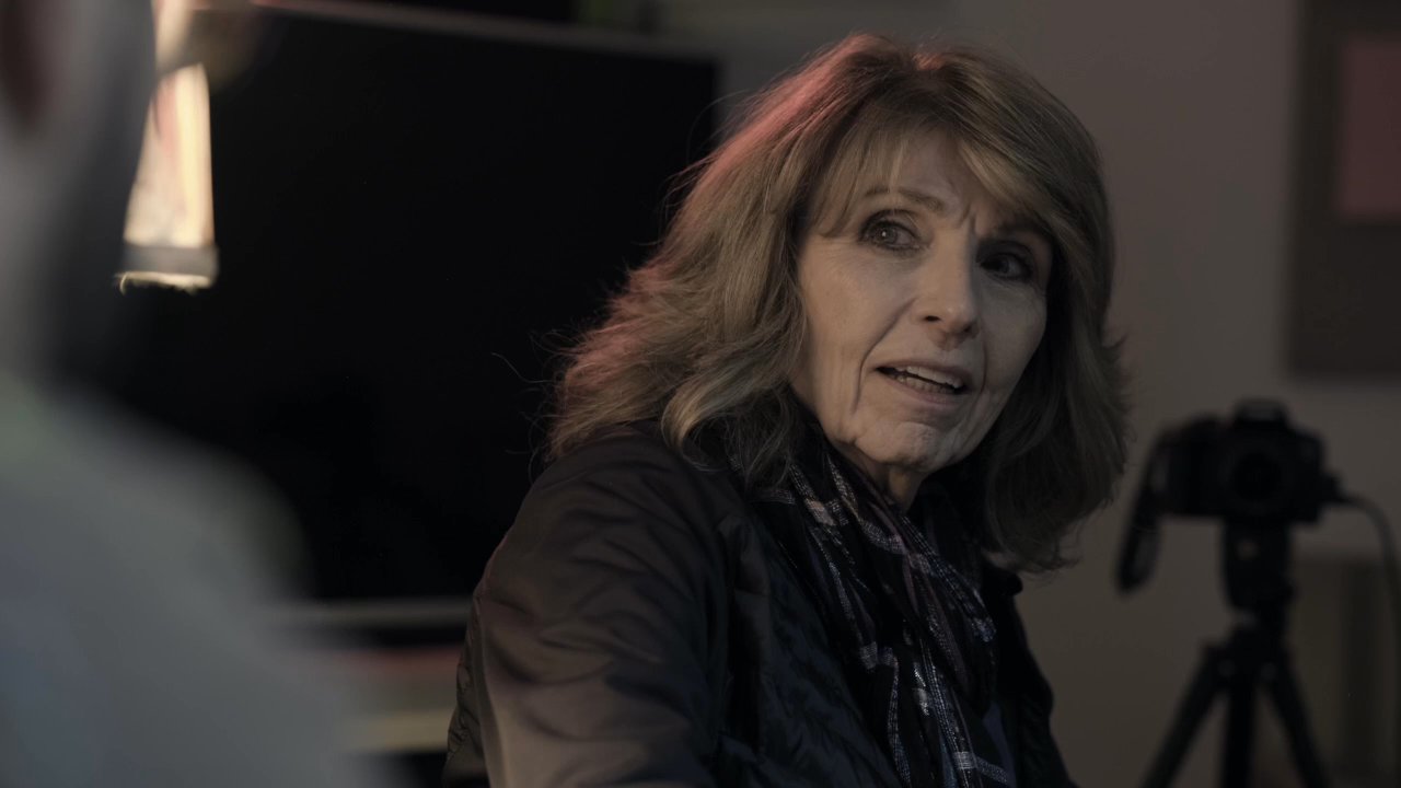 An adult man and woman engage in a focused, seated conversation within a studio environment equipped with filming gear. The interaction alternates between the two participants as they discuss their subject matter.