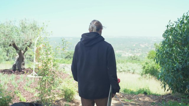 Guy walking through a field while holding a skateboard
