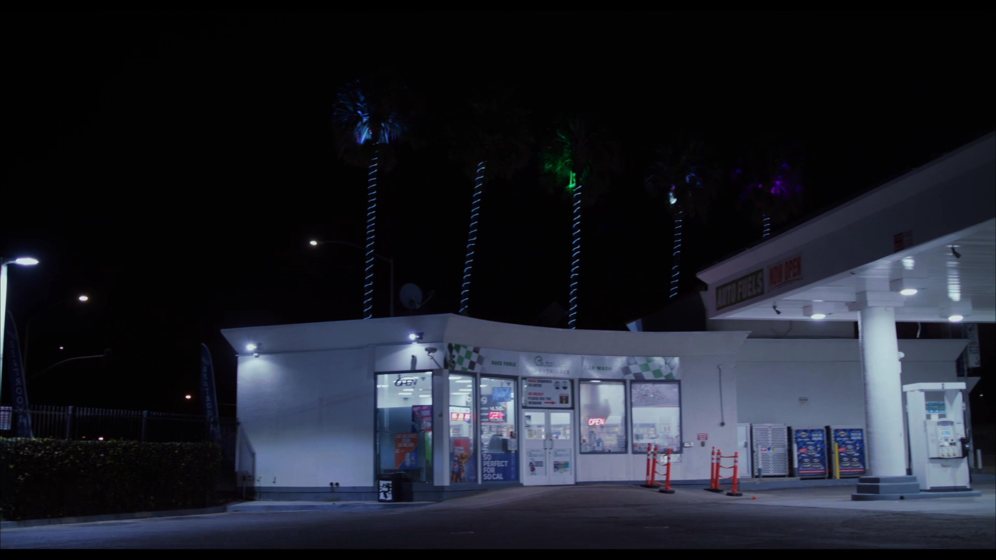A man pulls his white Jeep Renegade into a gas station at night and proceeds to wash the windshield with a squeegee.