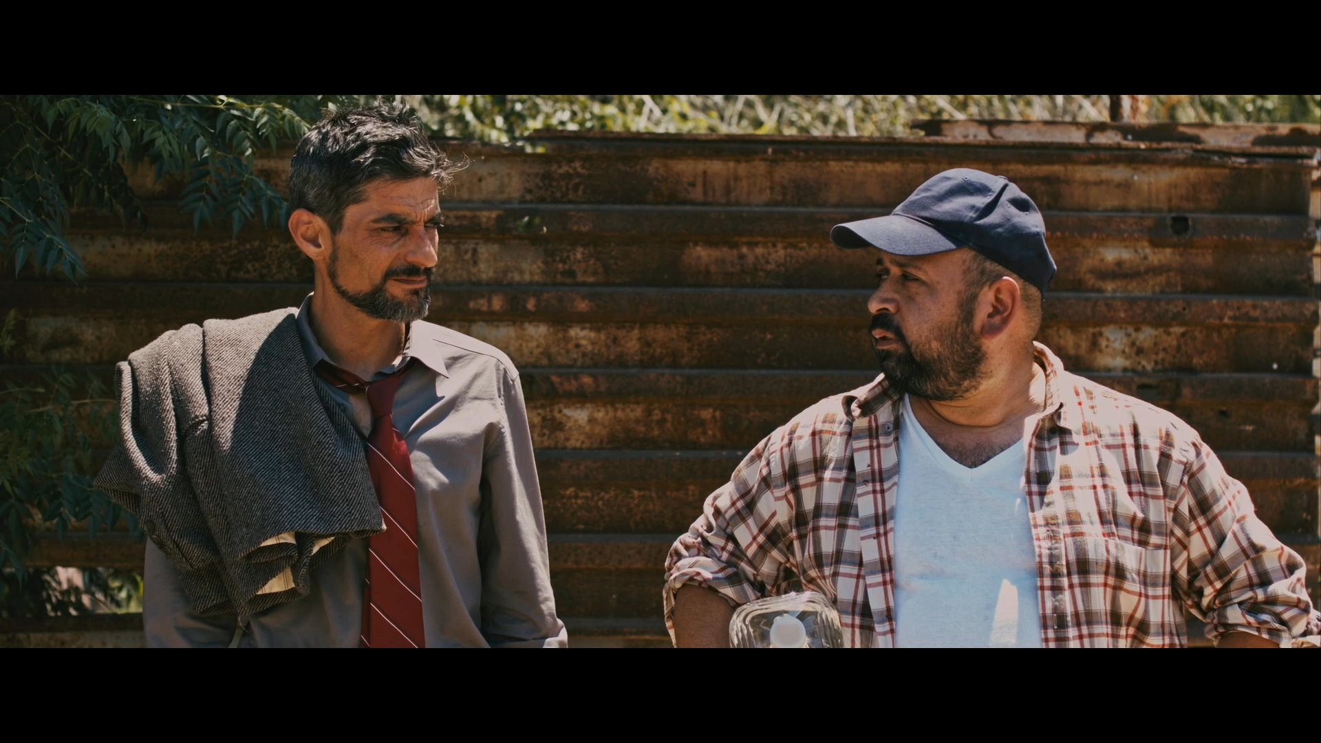 Two men stand outdoors discussing their next steps, with one ultimately deciding to follow the other on a long journey ahead. The exchange reflects a moment of contemplation and mutual agreement before they depart together.